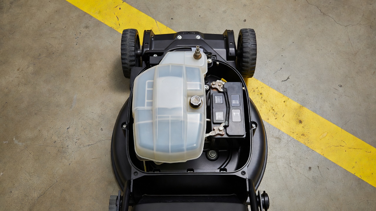 Close-up of a lawn mower engine showing fuel tank, oil drain, and battery — the hazardous components that ban it from dumpsters