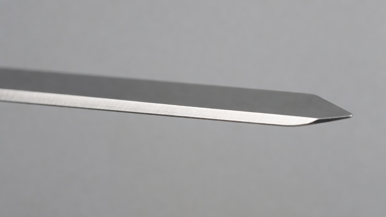Macro view of a new lawn mower blade showing the factory-ground beveled cutting edge