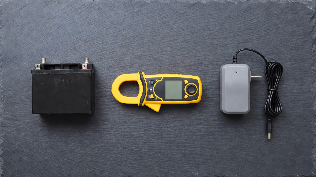 How Many Amps Does a Lawn Mower Battery Have? (Ah, CCA & Charging Amps Explained) Lead-acid battery, clamp meter, and battery charger arranged as three distinct amp-related concepts