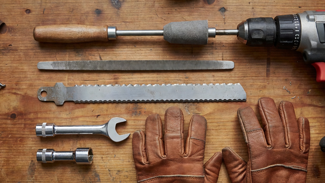How Much Does It Cost to Sharpen Lawn Mower Blades? (DIY vs. Professional Guide) DIY lawn mower blade sharpening tools laid out on a workbench including file, grinder attachment, wrench and gloves