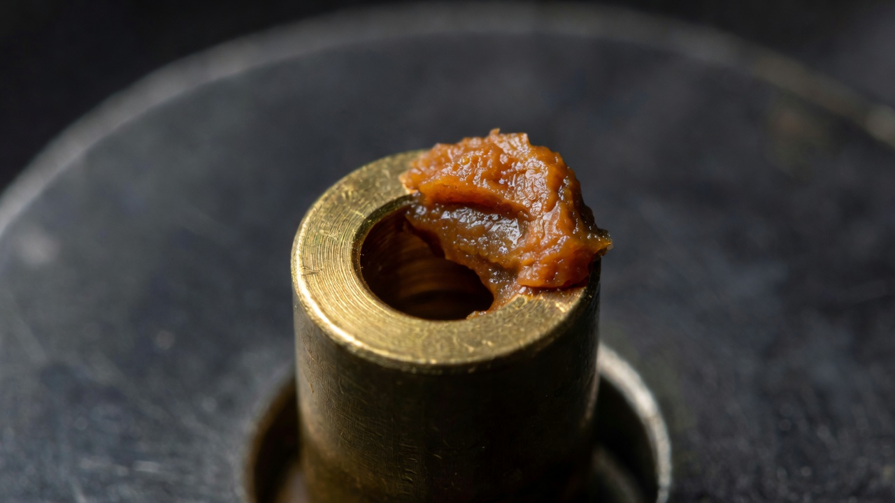 Macro view of a brass carburetor jet blocked by varnish deposit from stale fuel