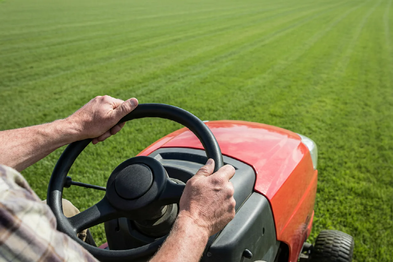How to Drive a John Deere Lawn Mower Hands on a riding mower steering wheel while driving across a lawn