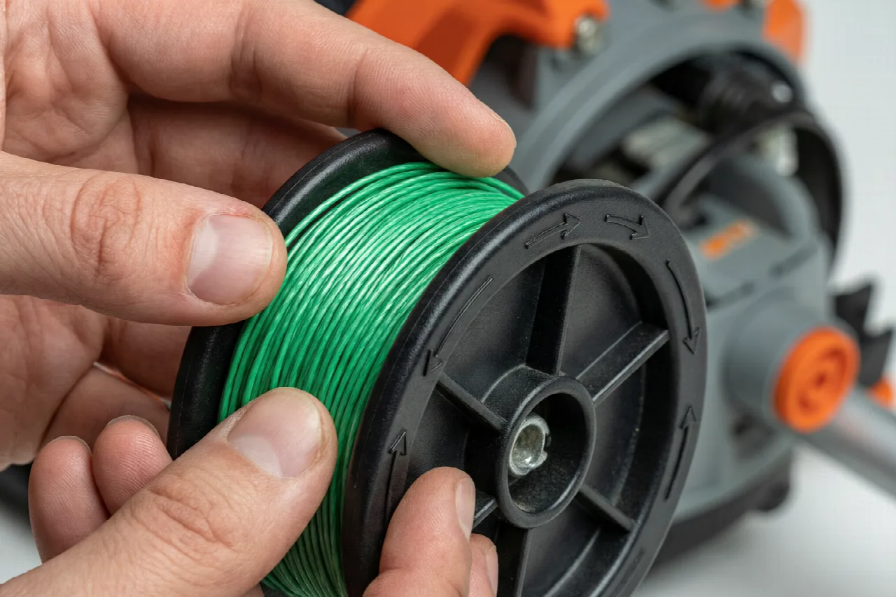 Hands winding trimmer line onto the inner spool of a weed eater head.