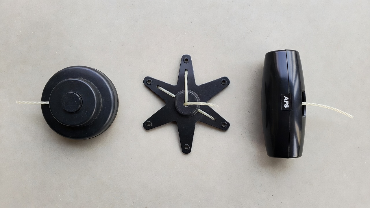 Three string trimmer head types side by side — bump-feed, fixed-line, and auto-feed — on a concrete surface