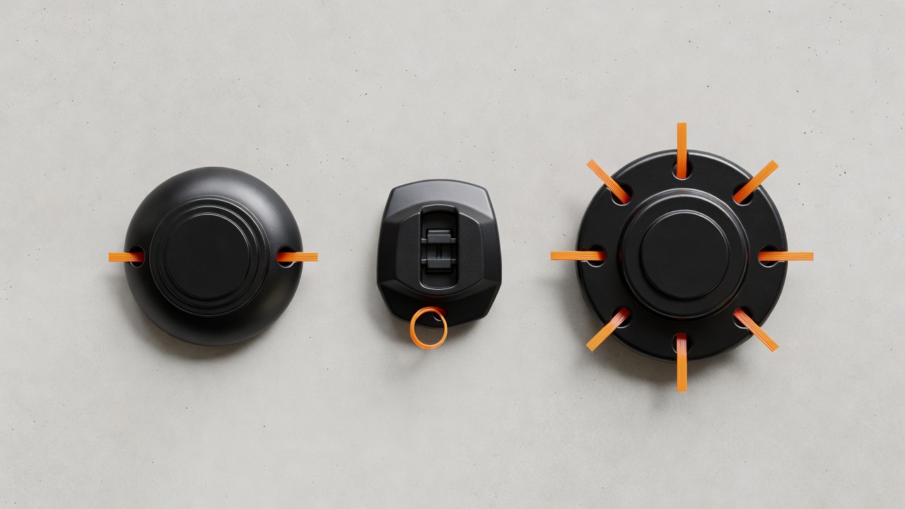 Three different trimmer head types laid flat on concrete showing different cap shapes and exit-hole configurations