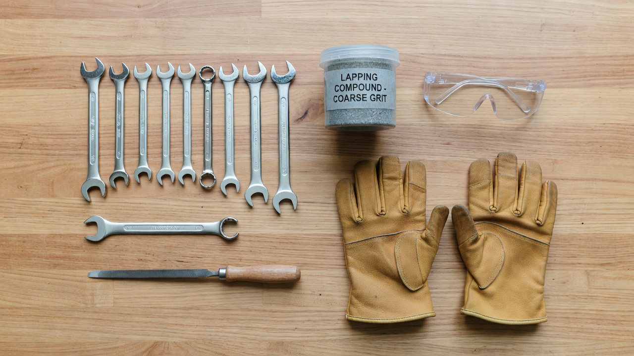An organized collection of tools including wrenches, lapping compound, and safety gear for mower maintenance.