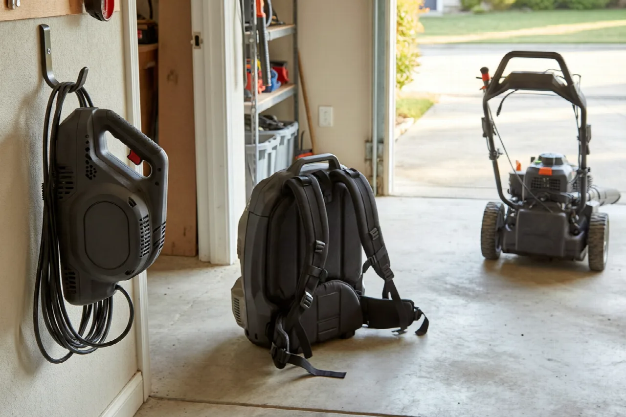 Handheld, backpack, and wheeled lawn blowers stored together at a garage doorway.