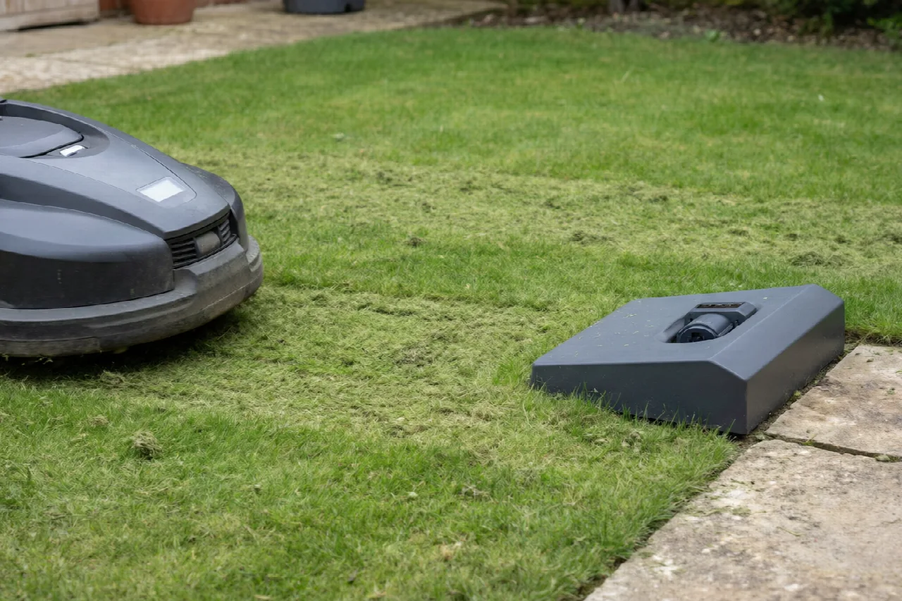 Robotic lawn mower approaching its outdoor charging station on short grass
