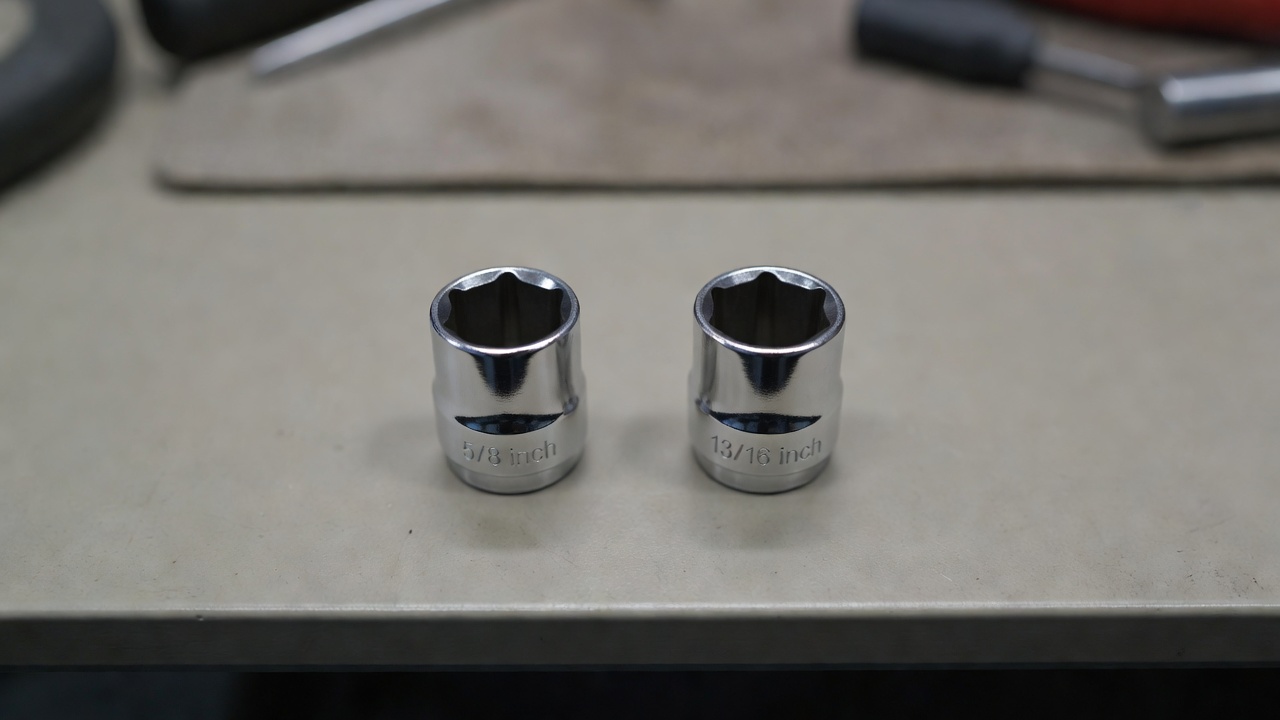 Two different sized spark plug sockets displayed on a workbench surface