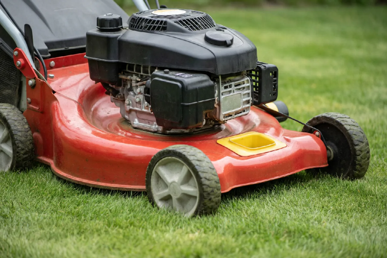 A gasoline walk-behind lawn mower on grass with its fuel cap clearly visible.