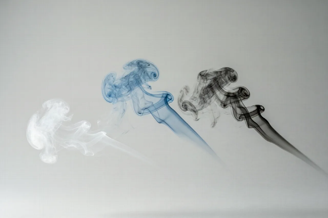 Why Is My Lawn Mower Smoking? Three wisps of smoke in white, blue, and black colors on a neutral background